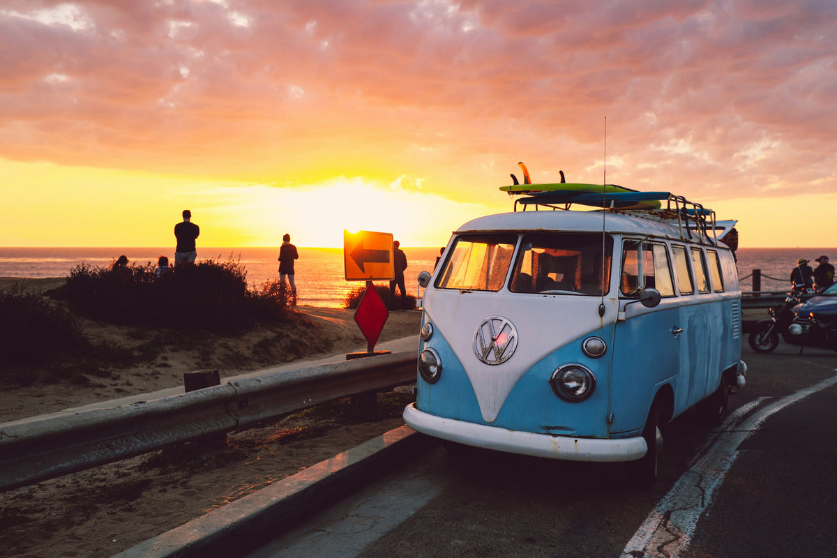 A vintage van carrying surfboards beside a coastal sunset